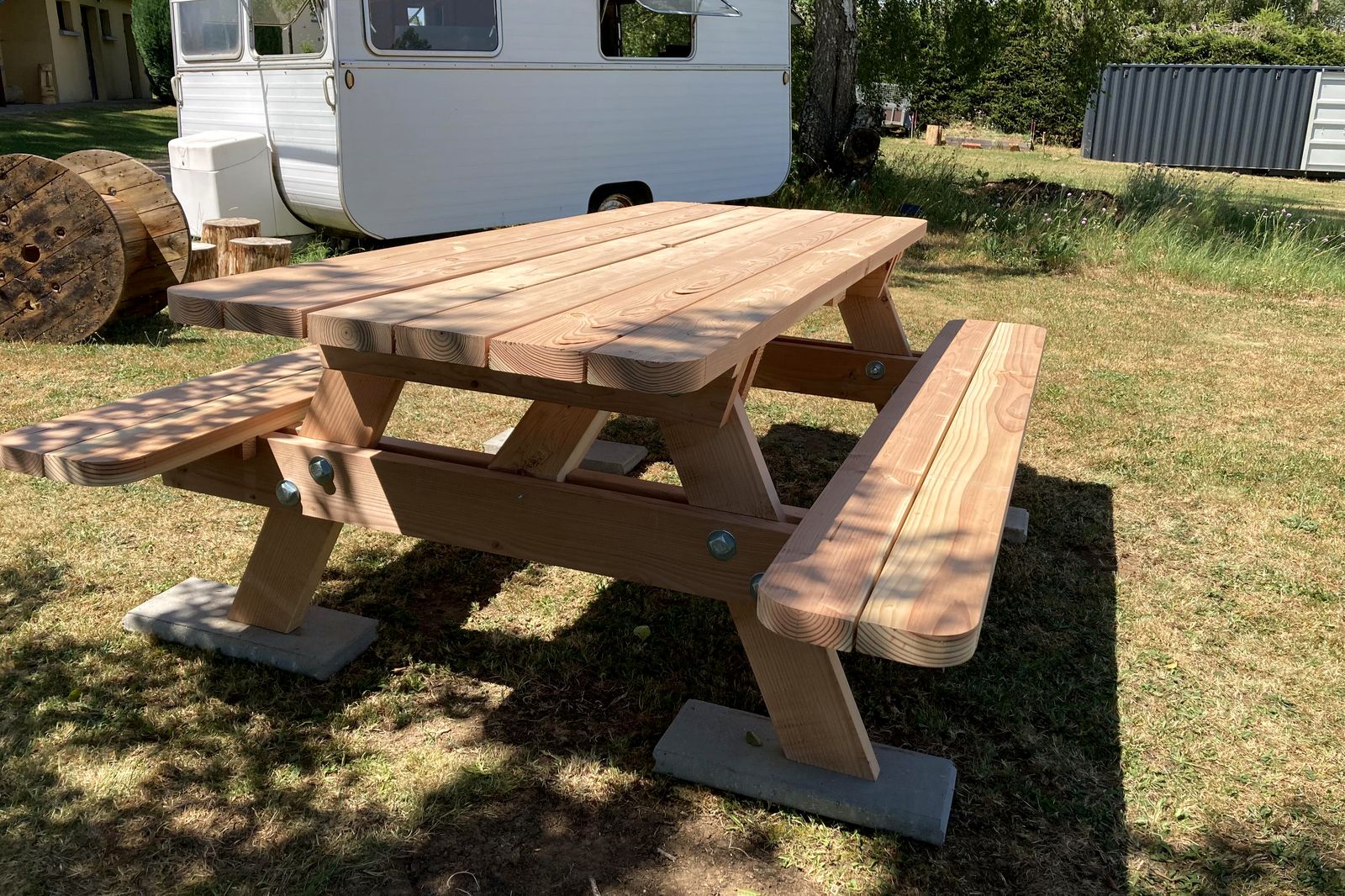 Table de pique-nique en Douglas massif sur un emplacement de camping, caravane vintage en arrière-plan